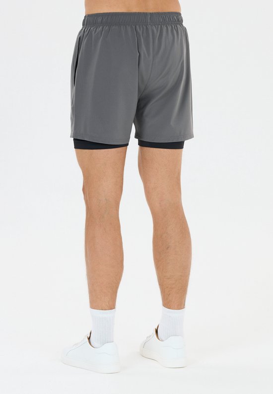 Van de achterkant gezien, een man met grijze sportshort en zwart binnenbroekje, witte sokken en witte schoenen.