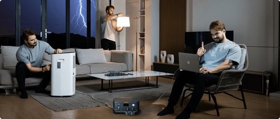 Donkergrijs Jackery Explorer 500 powerstation met oranje accenten, in een woonkamer waar een man werkt op een laptop en een lamp aanzet.