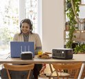 Donkergrijs Jackery Explorer 500 powerstation met oranje accenten, op een bureau naast een laptop en een glas sinaasappelsap.