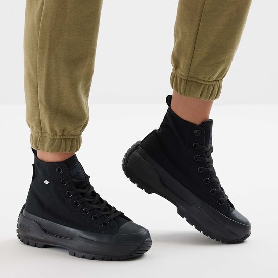 Een paar zwarte hoge canvas sneakers met dikke zolen gedragen met een groene joggingbroek.