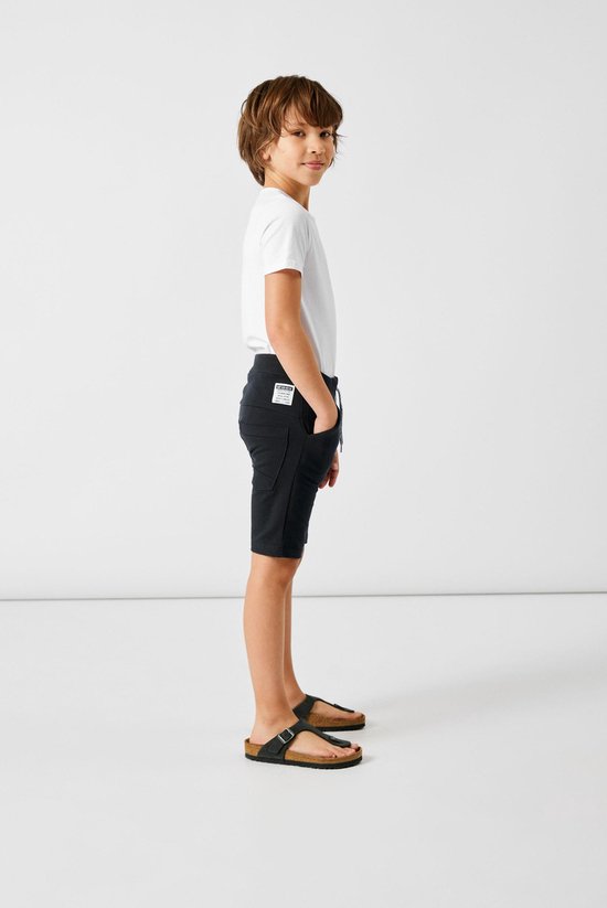 Jongen in een donkerblauwe short met een elastische tailleband, aantrekkoord en opgerolde broekspijpen.