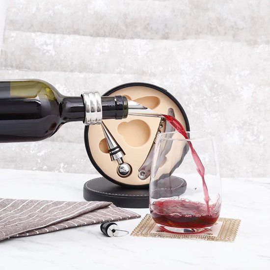 Wijn wordt in glas geschonken vanuit een fles met een zilverkleurige schenktuit, naast een ronde bewaardoos met wijnaccessoires.