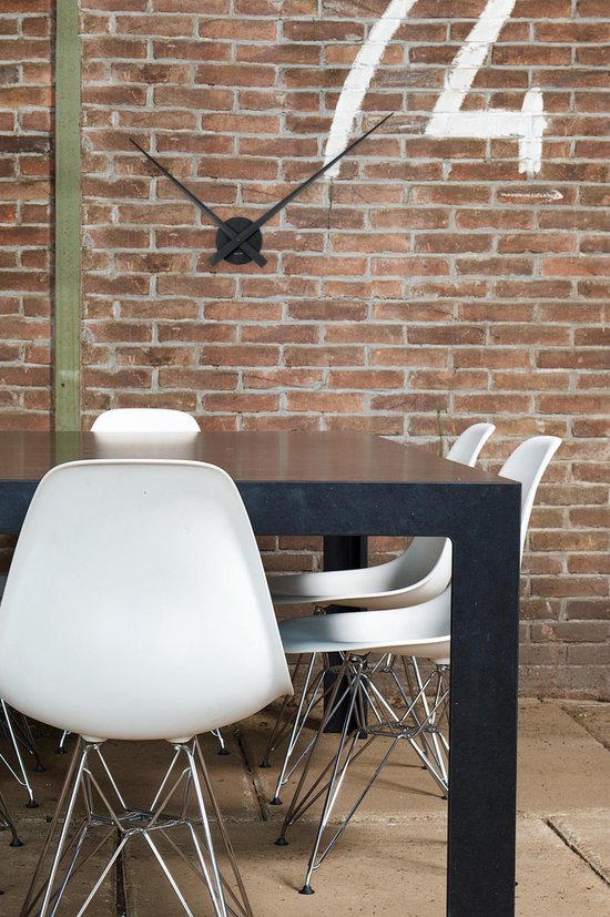 Horloge murale noire avec de longues aiguilles sur un mur de briques au-dessus d'une table.