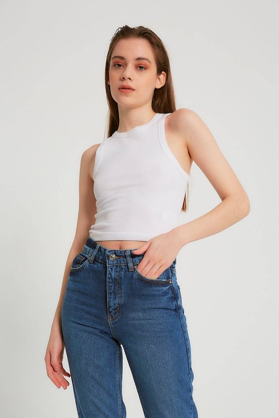 Model draagt een witte, geribbelde tanktop en een donkerblauwe spijkerbroek.