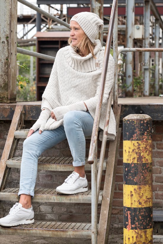 Vrouw met een off-white gebreide poncho, off-white muts en gebreide polswarmers.