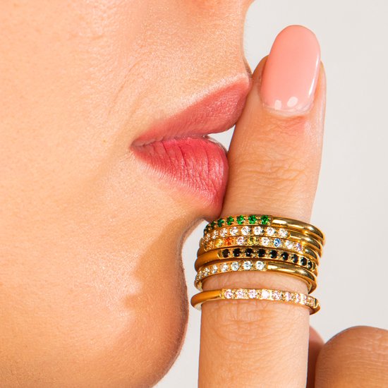 Vinger met stapelbare gouden ringen met gekleurde en zwarte steentjes.