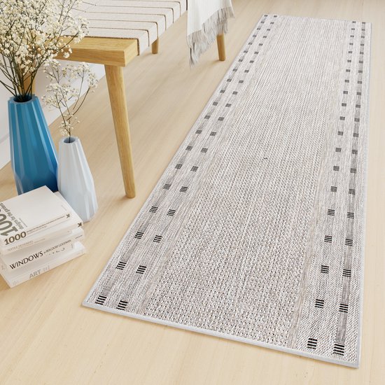 Tapis gris à motif de rayures noires sur un plancher en bois, à côté d'un banc et de plantes.