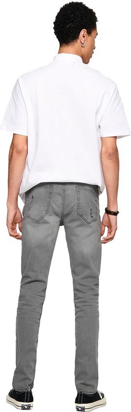 Achterkant van een man in grijze skinny jeans met scheuren en een wit T-shirt.