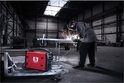 Rood Stamos lasapparaat in een industriële omgeving met vonken van het laswerk, met de lasser op de achtergrond.