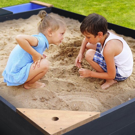 Twee kinderen spelen in een donkergrijze zandbak met houten hoeken.