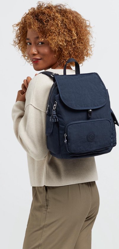 Vrouw met krullend haar draagt een donkerblauwe Kipling rugzak met klep en ritsvak op haar schouder.
