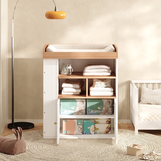 Witte commode met houten blad, aankleedkussen en geopende deurtjes met pakken luiers op de onderste plank.
