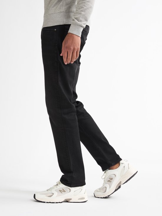 Model draagt een zwarte Petrol Industries regular tapered stretchdenim jeans met witte New Balance sneakers.