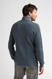 Man met donkerblauwe gemêleerde gebreide trui met hoge kraag en grijze jeans, gezien vanaf de achterkant.