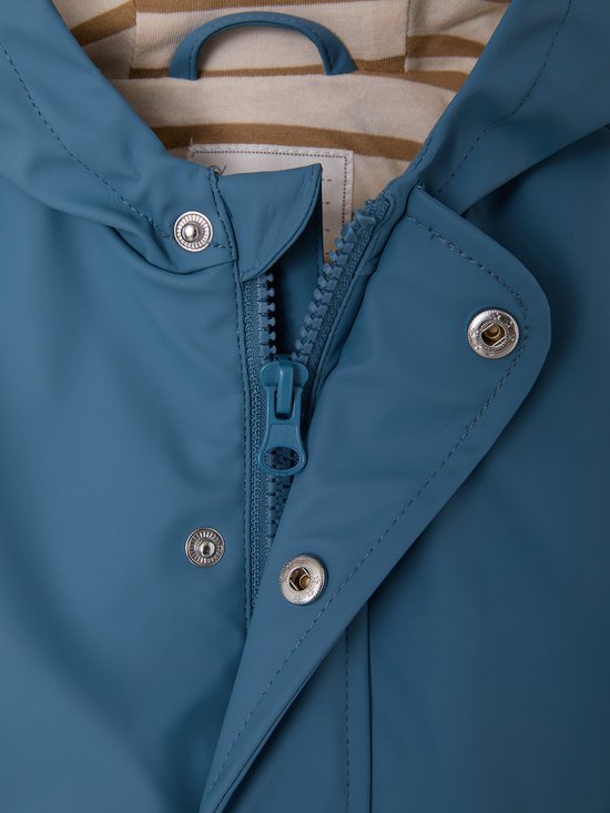 Detailopname van een blauwe regenjas met een rits, zilverkleurige drukknopen en een beige-bruin gestreepte voering.