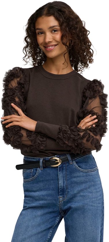 Model in bruine trui met doorschijnende, geruchede pofmouwen en jeans.