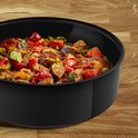 Zwarte hapjespan met stoofschotel van groenten, waaronder tomaten, aubergines en courgettes, op een houten achtergrond.