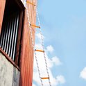 Een brandtrap met houten sporten en witte/blauwe touwen hangt naast een houten gevel.