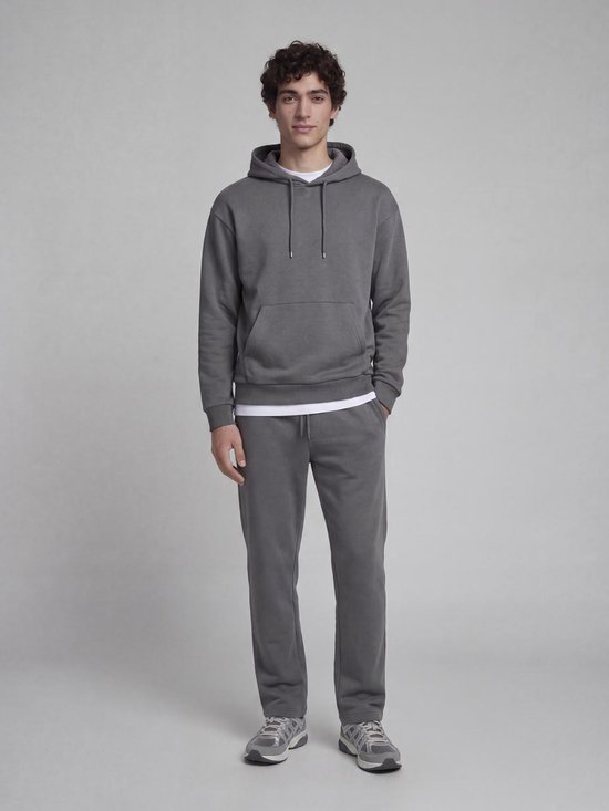 Model aan de voorkant, draagt een antracietgrijze hoodie met capuchon, witte onderlaag en bijpassende joggingbroek.