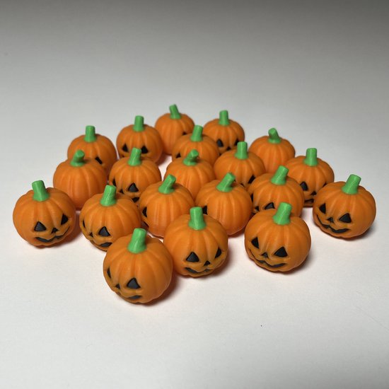 Groep kleine oranje 3D-geprinte pompoenen met groene steeltjes en zwarte, griezelige gezichten op een witte achtergrond.