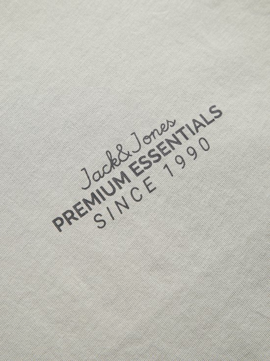 Close-up van de tekst 'Jack & Jones Premium Essentials Since 1990' gedrukt op de lichtgrijze stof.