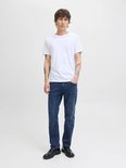 Man met tatoeages draagt een witte T-shirt en een donkerblauwe jeans.