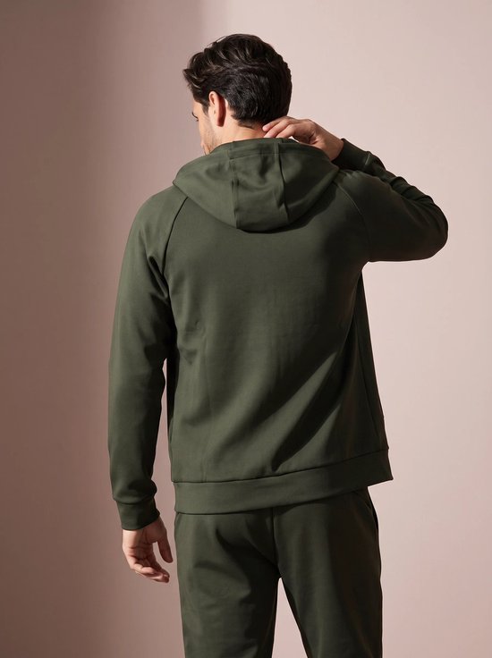 Man van achteren gezien, draagt een olijfgroene hoodie met capuchon en raakt zijn nek aan.