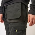 Close-up van de zwarte werkbroek met ruime zakken en geel detail.