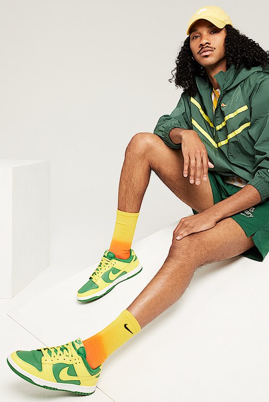 Model draagt groen-gele Nike Dunk Low sneakers, bijpassende outfit en sokken.