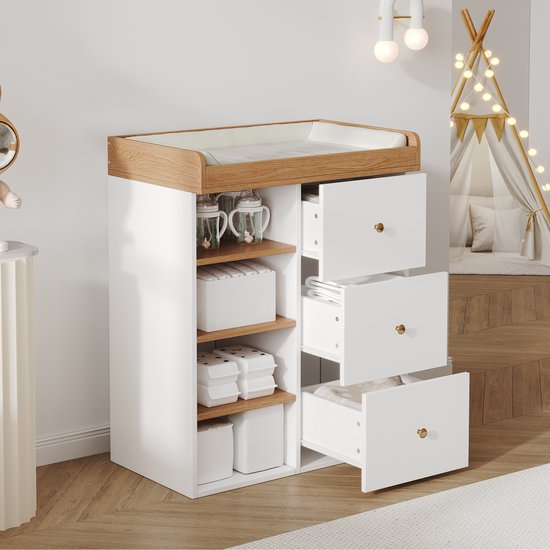 Close-up van een witte commode met houten bovenkant en drie lades die deels openstaan, gevuld met babykleding.