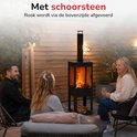 Zwarte buitenhaard met schoorsteen, brandend vuur en vakken voor hout. Mensen zitten op een terras.