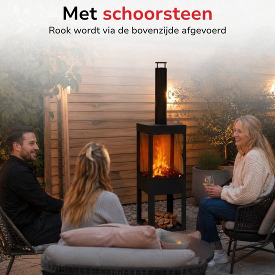 Zwarte buitenhaard met schoorsteen, brandend vuur en vakken voor hout. Mensen zitten op een terras.
