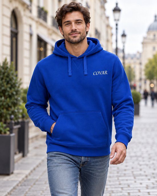 Model in koningsblauwe hoodie met capuchon en COVAR logo, lopend op straat.