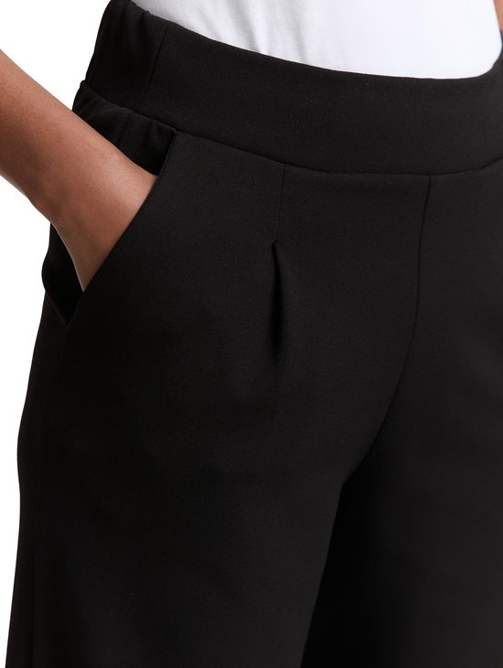 Model met hand in zak van zwarte broek met wijde pijpen en steekzakken.