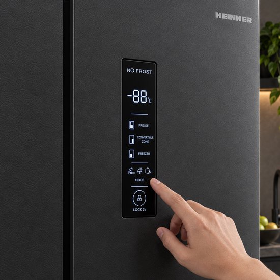 Donkergrijze Heinner koelkast met een touch display waarop '-88°C', 'FRIDGE', 'FREEZER', 'MODE' en 'LOCK 3s' wordt weergegeven. Een vinger drukt op de 'MODE' knop.