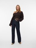 Model met lang bruin gebreid vest, donkerblauwe wijde jeans, beige top en slangenprint pumps.