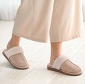 Voeten in lichtroze pantoffels met crèmekleurige pluches voering, gedragen op een lichte houten vloer.