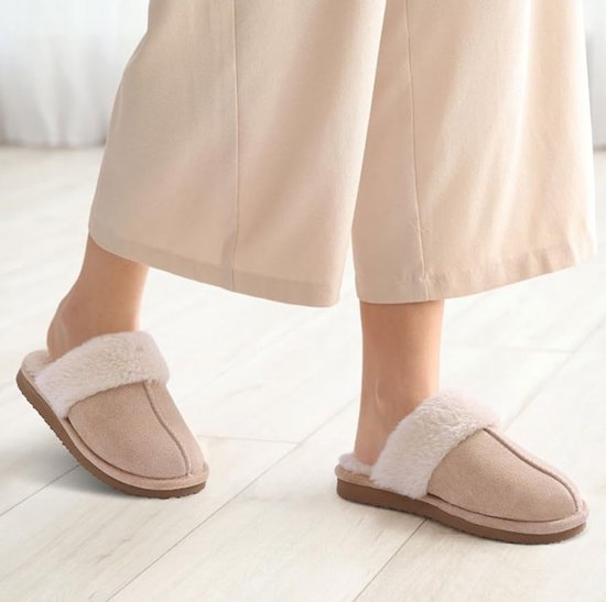 Voeten in lichtroze pantoffels met crèmekleurige pluches voering, gedragen op een lichte houten vloer.