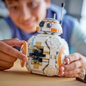 Un enfant construit un droïde BB-8 LEGO blanc et orange avec des pièces mécaniques visibles.