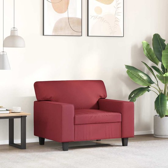 Wijnrode kunstleren fauteuil naast een houten bijzettafel met plant, in een lichte woonkamer.