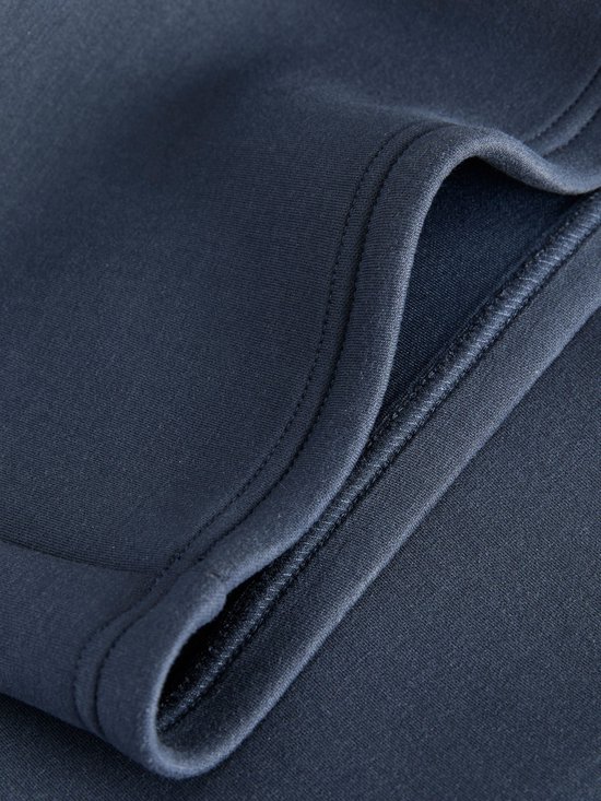 Detail van de doorgestikte zakrand van de donkerblauwe broek.