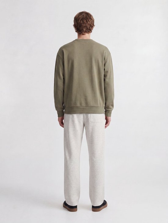 Achteraanzicht van een man in een olijfgroene trui en lichtgrijze joggingbroek met achterzak.