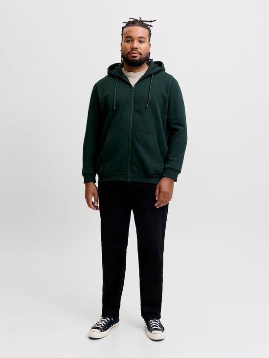Model in een donkergroen JACK & JONES vest met rits, zwarte broek en sneakers, staand op een witte achtergrond.