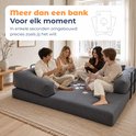 Vier personen zitten op een blauwe corduroy slaapbank en spelen een kaartspel.