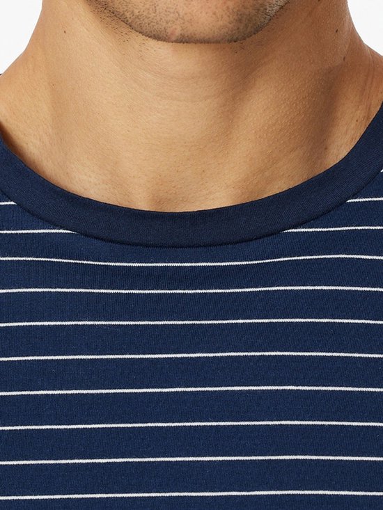 Detail van een marineblauw T-shirt met dunne horizontale witte strepen en een ronde hals bij een model.