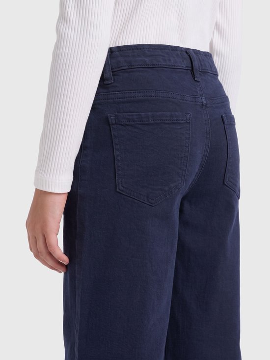 Achterkant van een marineblauwe jeans met wijde pijpen en achterzakken, gedragen met een witte top.