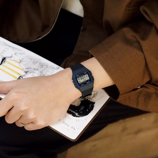 Montre Casio noire au poignet tenant un carnet, portée avec une veste marron.