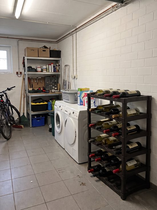 Hoog zwart kunststof wijnrek met meerdere flessen in een kelder naast een wasmachine.