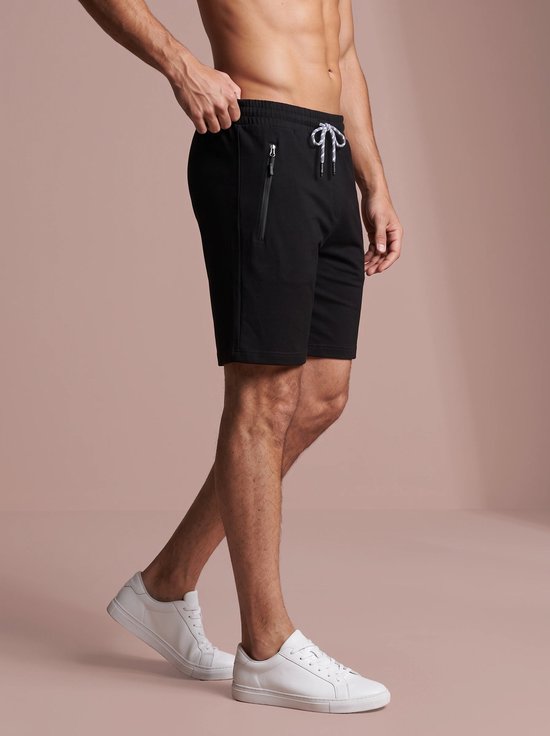 Profiel van een man in een zwarte sportshort met ritszak en witte sneakers.