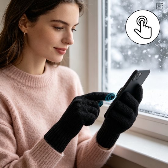Vrouw in roze trui draagt zwarte touchscreen-handschoenen terwijl ze een smartphone bedient bij een besneeuwd raam.